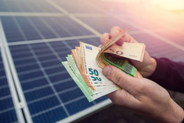 Siyahlı güzel genç eller güneş panelleri önünde avroyu tutuyor. Yeşil elektrik kavramı