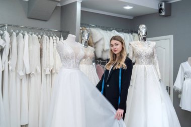 female consultant in a store measures a wedding dress with measuring tape