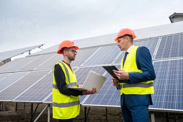 handsome young guys in hard hats with documents stand near the newly installed panels. Green electricity concept