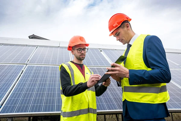 the director of a large company inspects the work of an employee in special clothing installed solar panels. The concept of saving green electricity