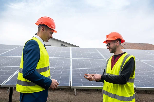 two professionals in workwear discuss solar panels and their impact. The concept of green electricity and its impact