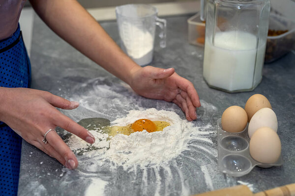 Beautiful young female hands break eggs into flour to knead a beautiful dough. Cooking concept