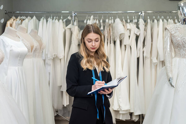 pretty young saleswoman hold notes diary in modern wedding store. Female bridal store  