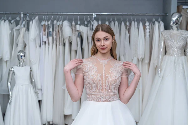 Beautiful happy young female tailor is trying on an elegant wedding dress in bridal Boutique