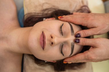 Güzel esmer, güzel saçlı bir kız güzel bir yüz masajının üzerinde yatıyor. Yüz masajı kavramı