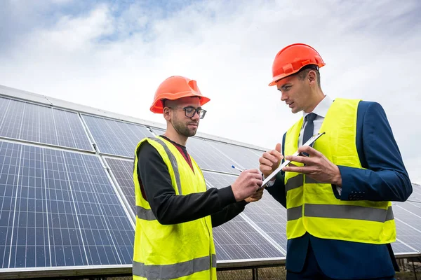 new young professionals in professional helmets and special clothing are discussing a plan to install solar panels. The concept of installing green electricity