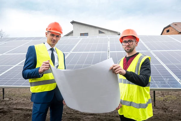 tall men in work clothes are considering whether to install solar panels in the open air. The concept of caring for solar panels under the sky