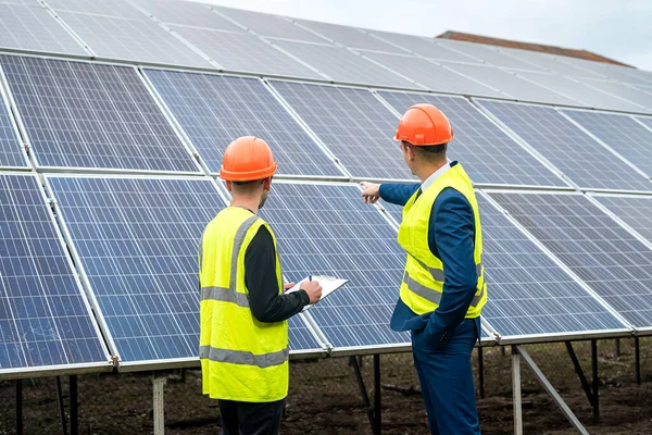 two young workers in overalls and helmets check the installed solar panels. Green electricity concept