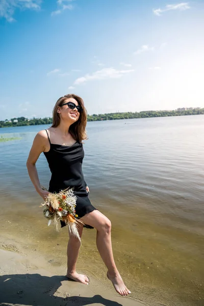 若い女性は裸足で川に立っています 黒のドレスの可愛い女の子は夏の日を楽しむ — ストック写真