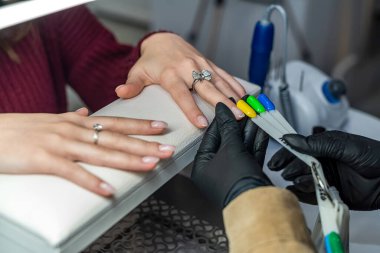 Manikür ustası kabinedeki müşteri için jel rengini seçin. Renkli sunucuların paleti