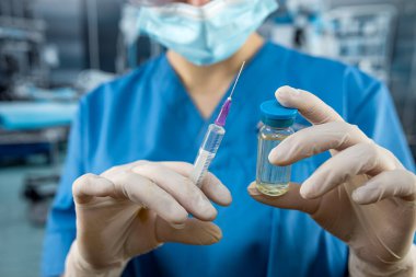 Üniformalı kadın doktor portresi, eldivenler yüz maskesi ameliyathanede antibiyotikle hazırlanmış şırınga. Sağlık hizmeti konsepti. Ameliyat için hazırlama