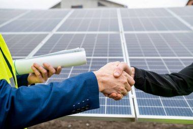 Tulum ve kask takmış iki işçi panel planını tamamladıktan sonra el sıkışıyor. Yeşil elektrik kavramı
