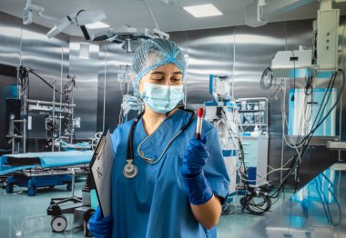 Koruyucu formalı eldiven şapkalı ve maskeli genç hemşire ameliyathanedeki ve hastanedeki kan örneklerine bakıyor.