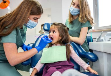 Güzel kadın dişçi, tıbbi üniformalı asistanıyla çocukların dişlerine bakıyor. Çocuk dişlerinin tedavisi konsepti