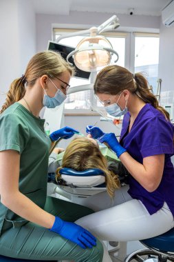 Diş sağlığı kliniğinde yetişkin dişlerini tedavi eden ayna, matkap ve diş suyu spreyi kullanan dişçiler.