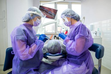 Koruyucu takım elbiseli ve gözlüklü bir doktor ultraviyole lamba kullanarak dişçilikte profesyonel bir prosedür yapar. Temizlik ve diş bakımı