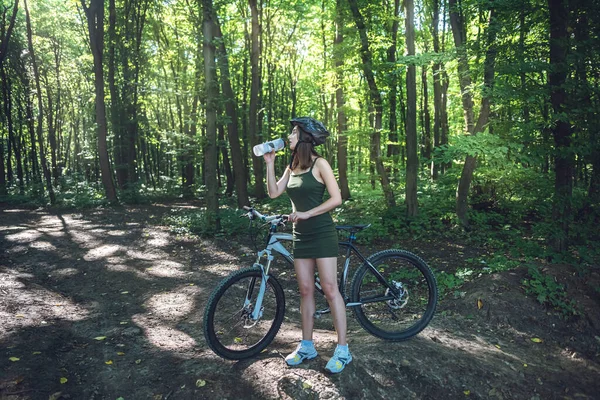 Fitness girl wear green dress rides a modern mountain bike in forest at hot summer day. Activity freedom and relaxation lifestyle
