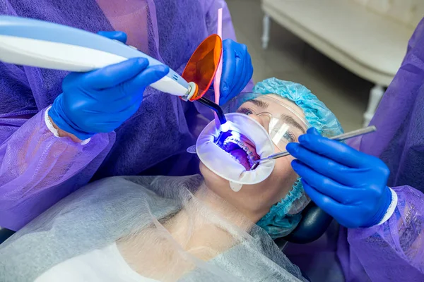 the dentist with his assistant in overalls uses UV lamps, then treats patients\' teeth. Tooth restoration concept