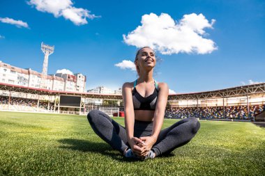 Stadyumda yeşil çimlerle yoga yapan atletik bir kadın. spor başarısı
