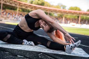 Sağlıklı bir kadın, stadyumun dışında paspasın üzerinde geriniyor. Sağlıklı yaşam tarzı kas esnekliği kavramı