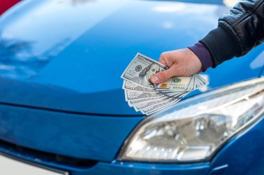 male hands in a business suit hold dollars on a background of blue beautiful car. Business concept. The concept of buying a car.