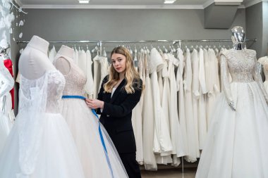 Kadın terzi, santimetre bant ile düğün salonunda çalışıyor. Beyaz zarif elbiseyi ölçüyor.