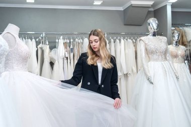 Güzel gelin, düğün butiğinde beyaz gelinliklere bak ve dokun.