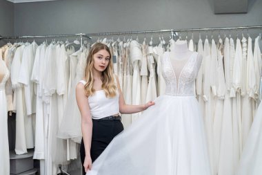 Güzel gelin, düğün butiğinde beyaz gelinliklere bak ve dokun.