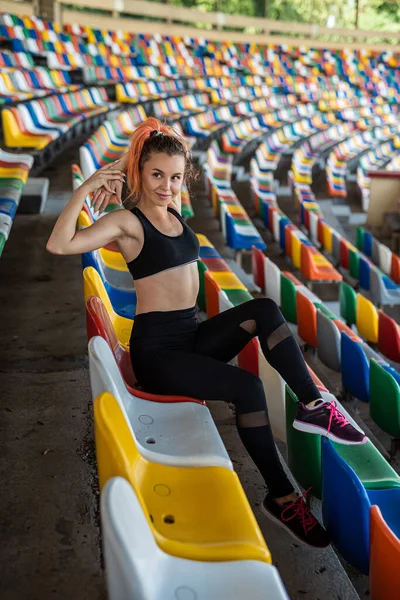 beautiful sporty woman coach doing exercises with colored chairs in the stadium, active lifestyle