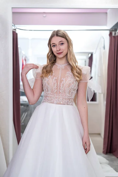 The young bride tries on an elegant wedding dress and pose in the salon. The concept of the happiest day in life
