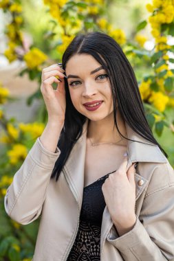 Beyaz jaketteki güzel kız doğanın tadını çıkarıyor bahar bahçesinde çiçek açan ağaç dallarının altında duruyor.