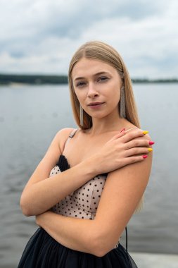 Gökyüzü ve suyun arka planında uzun siyah elbiseli güzel genç bayan, özgürlük.