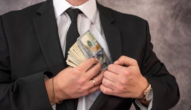 İşadamı, pahalı takım elbisesinin cebine dolar banknot parası koyuyor. İş ve kâr kavramı