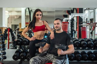 Modern spor salonundaki erkek çalıştırıcının kontrolünde bir halterle çalışan formda bir bayan müşteri. Yaşam tarzı olarak spor
