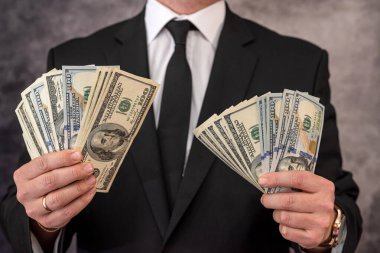 Yakışıklı nüfuzlu bir adam şık bir şekilde giyinmiş ve önünde dolar şeklinde para kazanıyor. İş adamı kar kavramı