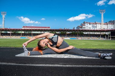 Esneme hareketleri yapan sportif bir kadın ya da stadyum pistinde yoga egzersizi yapan. Esneklik kavramı