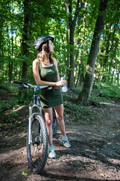 Young sexy woman wear green short dress rides a bicycle in the forest, spend free time on summer day. Activity lifestyle