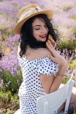 Hasır şapkalı güzel genç kız lavanta tarlasının arka planında oturuyor.