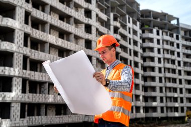 handsome young worker in uniform and helmet holds in his hands a detailed plan on the construction site. Construction concept