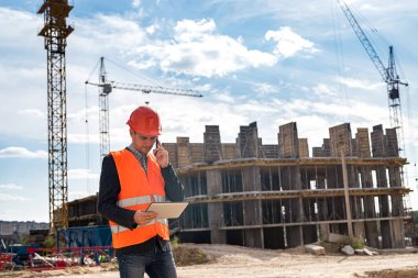Üniformalı ve miğferli genç bir işçi inşaat detaylarını öğrenmek için patronu arıyor. İnşaat konsepti