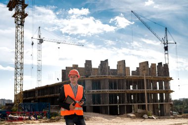 Üniformalı ve kasklı bir işçi yeni binanın arka planında tabletine bakıyor. İnşaat konsepti