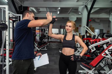 A handsome young trainer with a good figure trains a young client who came to the gym. The concept of overweight