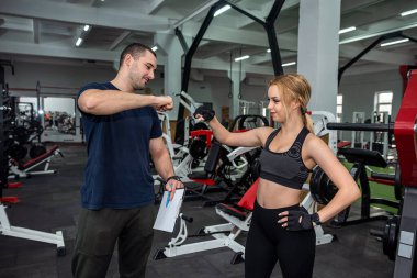Erkek antrenör, spor salonunda ağır halterlerle egzersiz yapan zayıf kadın müşterisine yardım ediyor. Sağlık konsepti için spor ve spor
