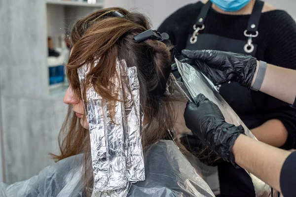 a young girl is sitting in a comfortable chair in a beauty salon where her beautiful hair is dyed. Beauty salon concept during a pandemic