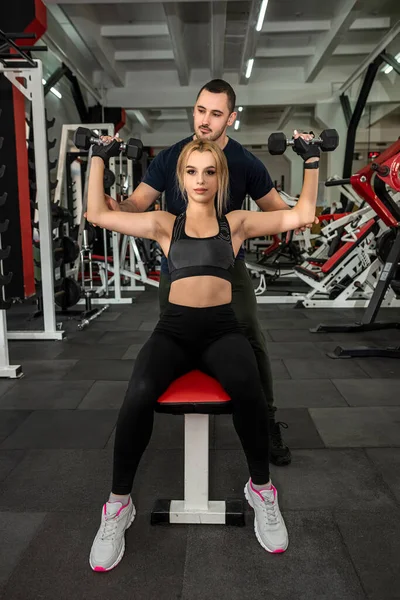 Erkek antrenör, spor salonunda ağır halterlerle egzersiz yapan zayıf kadın müşterisine yardım ediyor. Sağlık konsepti için spor ve spor