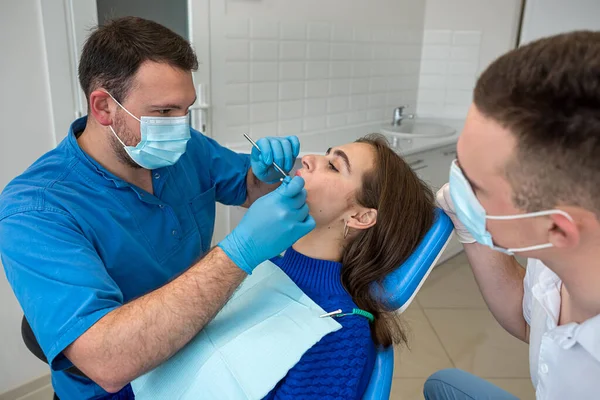 dentists with mirror, drill and dental air water gun spray treating adult patient teeth at dental clinic