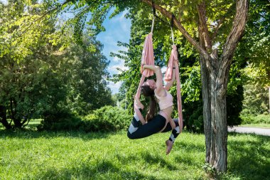 Genç atletik yoga eğitmeni dışarıda ağacın altında antrenman yapıyor. Ağaçların altındaki tuvallerde yoga eğitimi kavramı..