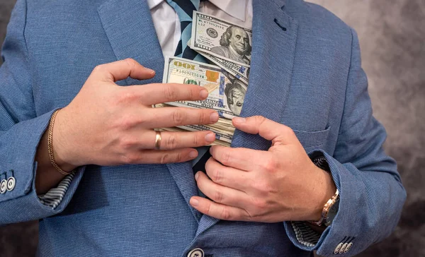 a man with a strong physique in a shirt and jacket holds his own earned dollar bills. The concept of a good big profit in dollars