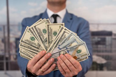 handsome influential man stylishly dressed holding earned money in the form of dollars in front of him. Businessman profit concept