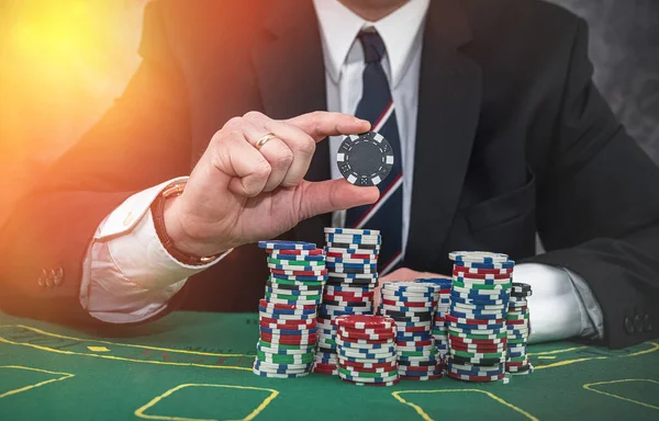 Male hand holding poker chips in casino green felt. Gambling concept